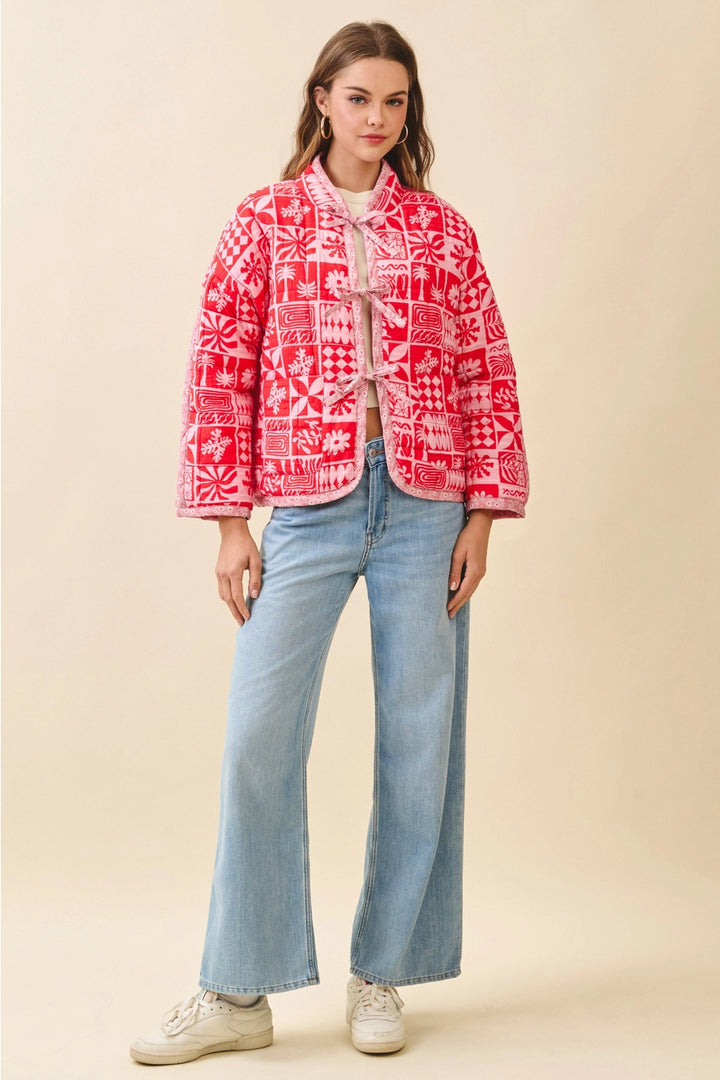 Woman wearing a red patterned jacket and light blue jeans on a beige background