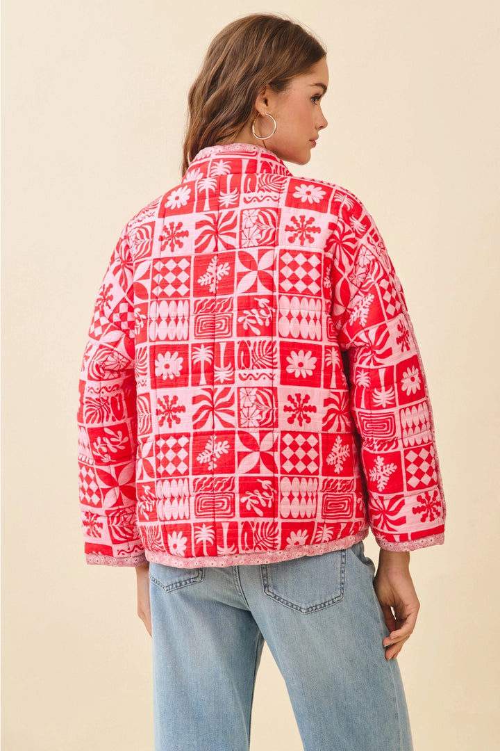 Person wearing a red and white patterned jacket with blue jeans on a beige background